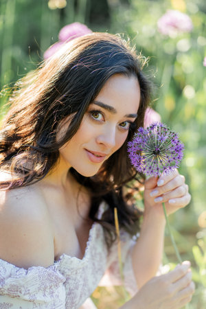 Portrait of a young dark-haired woman near flowers in the park. Happy model in a romantic dress rejoicing in spring.の写真素材