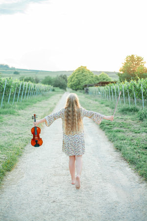 Closeup of a little girl with long blond hair playing the violin outdoor. Child holding a musical instrument in her hands. In nature.の写真素材