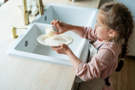 little girl of 7 years old washes a plate in the kitchen near the sink. Child cleans the dishes. ecofriendly.の写真素材