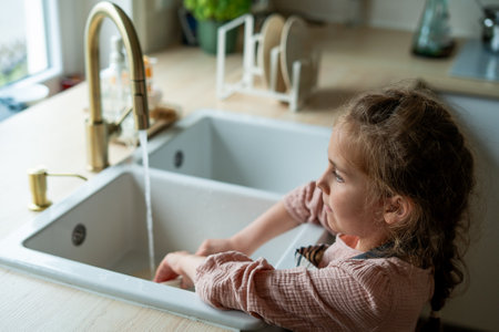 Closeup of children's hands washing a plate near the sink in the kitchen. Little girl holding an ecofriendly dishwashing brush.の写真素材