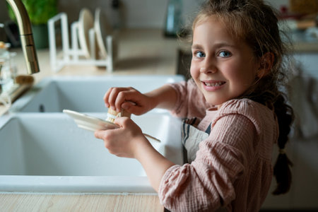 little girl of 7 years old washes a plate in the kitchen near the sink. Child cleans the dishes. ecofriendly.の写真素材