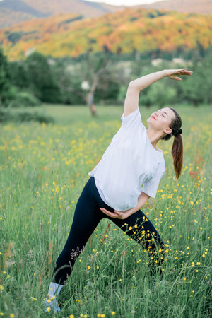 Pregnant young woman in sportswear doing yoga on the street outside the city. Therapeutic sports in the park. Motherhood. Meditation.の写真素材