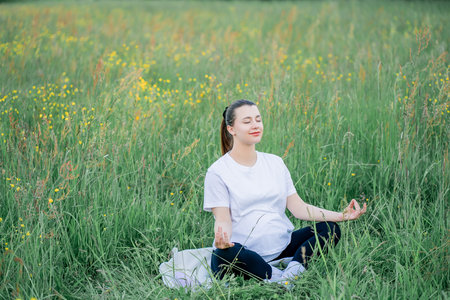 Pregnant young woman in sportswear doing yoga on the street outside the city. Therapeutic sports in the park. Motherhood. Meditation.の写真素材