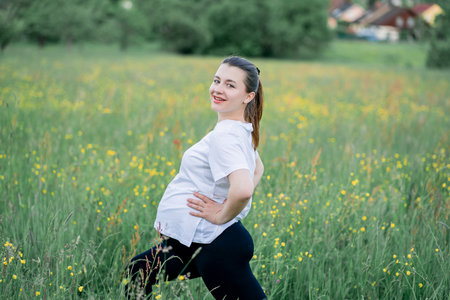 Pregnant young woman in sportswear doing yoga on the street outside the city. Therapeutic sports in...