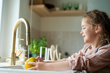 Little cute girl of 7 years old washes vegetables under the tap in the kitchen. Healthy food. Cooking.の写真素材