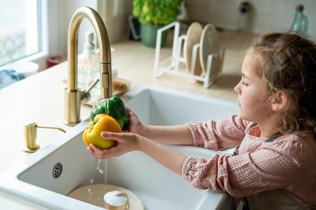 Little cute girl washes vegetables under the tap in the kitchen.の写真素材