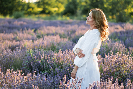 Beautiful woman enjoying summer breeze in lavender field. Portrait of blonde in sunlight.の写真素材