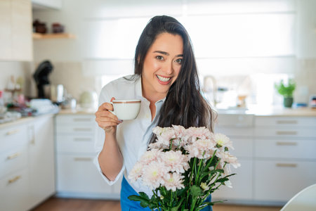 Young woman with brown hair drinking hot coffee at home in a bright kitchen.の写真素材