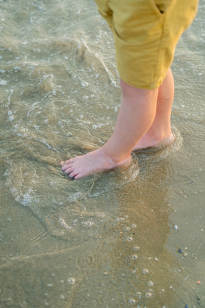 Closeup of children's feet near the sea. Beach with sand. Blue water. Sea vacation.