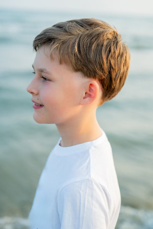 Portrait of a smiling boy of 10 years old near the sea at sunset. Child on the beach. Sea vacation.