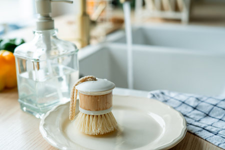 Plate with an ecobrush for washing dishes near the sink, detergent in a glass bottle, a towel....