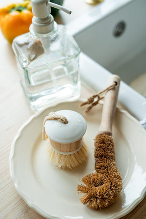 Plate with an ecobrush for washing dishes near the sink, detergent in a glass bottle, a towel....