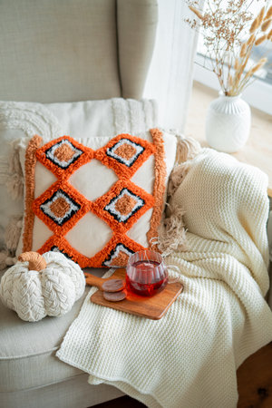 Cup of hot spiced tea, chocolate chip cookies, autumn decor with pumpkins, a cozy chair with a blanket and pillows by the window.の写真素材