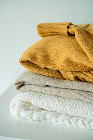 Warm cozy clothes on chest of drawers in home interior. Knitted autumn sweaters. Organization.