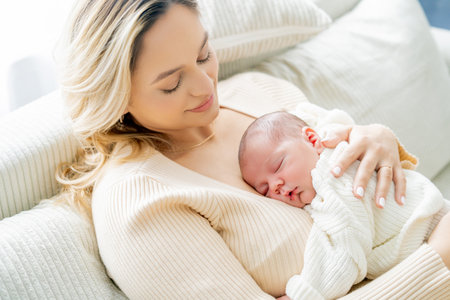 Young mother tenderly holds newborn baby in her arms at home. healthy motherhood.
