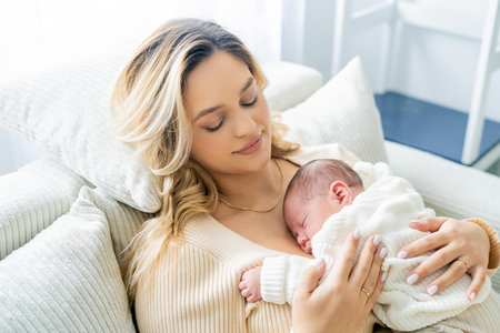 Young mother tenderly holds newborn baby in her arms at home. healthy motherhood.