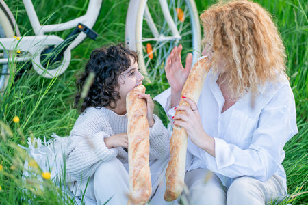 Red-haired mother with little daughter enjoying life in the field with bicycle and picnic. Eating baguette.の写真素材