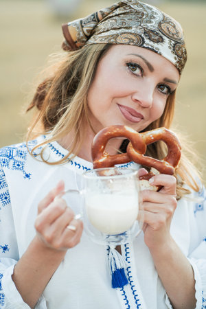 Portrait of a blonde woman in comfortable clothes and a scarf, 40 years old, in a field with hay bales, enjoying the evening, drinking milk and eating pastries.の写真素材
