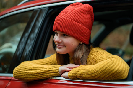 Portrait of a teenage girl in the window of a red car against the background of an autumn forest.