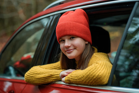 Portrait of a teenage girl in the window of a red car against the background of an autumn forest.