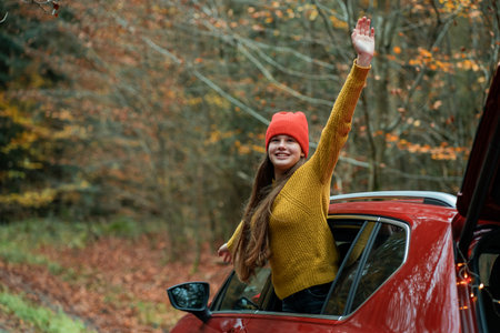 Portrait of a teenage girl in the window of a red car against the background of an autumn forest.
