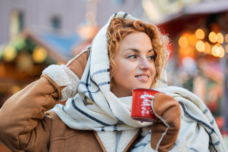 Red haired happy woman drinking hot mulled wine in red cup at Christmas market. Enjoying winter holidays.の写真素材