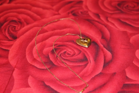 A golden pendant in the shape of heart on the rose backgroundの写真素材