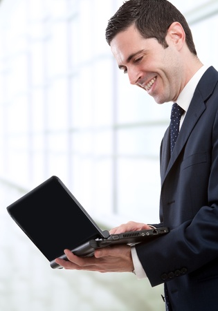 Handsome young business man in blue suit stamding with laptop in office.の写真素材