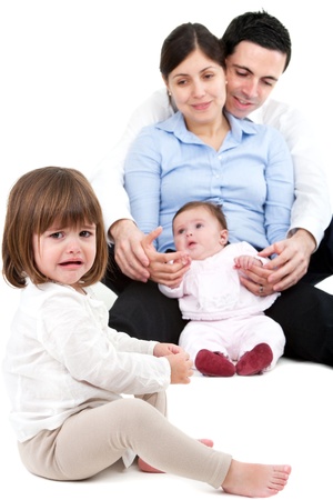 Unhappy jealous little girl crying with her family in background.の写真素材