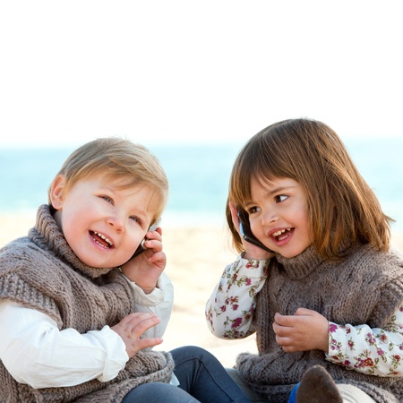 Portrait of two cute little girls o beach talking on mobile phones の写真素材