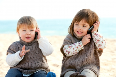 Portrait of two cute little girls on beach having conversation on mobile phones の写真素材