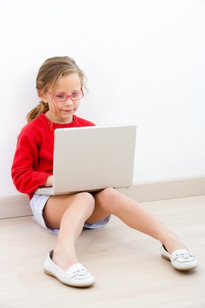 Portrait of cute blond girl doing homework at home with laptop  の写真素材