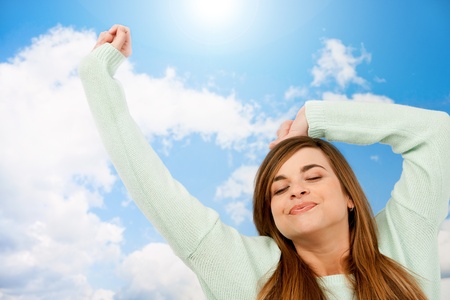 Young woman with eyes closed stretching arms on blue sky の写真素材