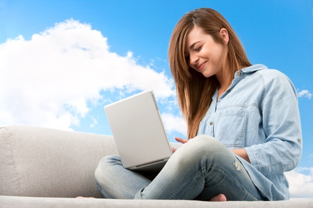 Young attractive woman sitting on couch with laptop Blue sky background の写真素材