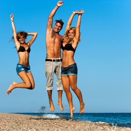 Three attractive energetic friends jumping on beach  の写真素材
