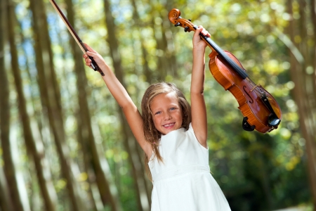 Portrait of happy violinist raising violin in the woods.の写真素材