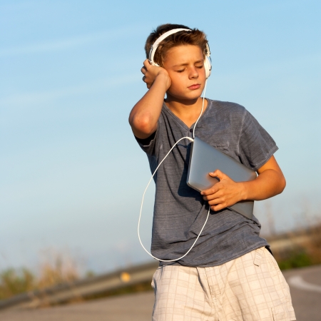 Handsome teen boy enjoying music on tablet outdoors の写真素材