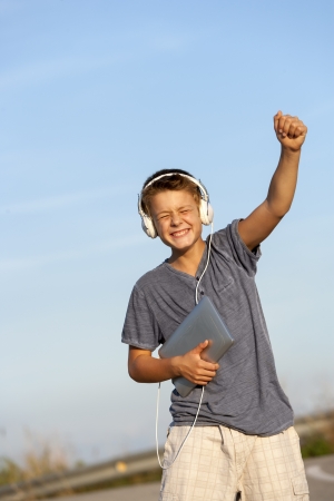 Cute boy dancing to the rhythm with headphones and digital tablet outdoors の写真素材