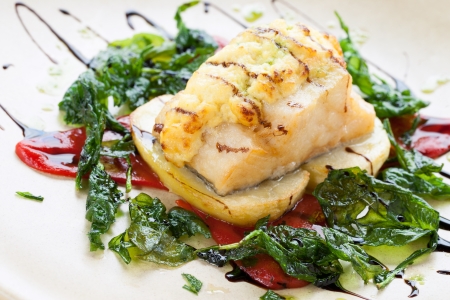 Close up of cod fish with potatoes and spinach leaves.