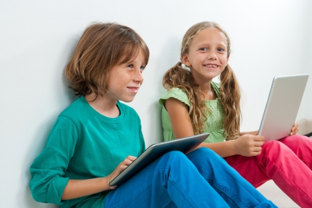 Portrait of two kids sitting with laptop and digital tablet indoors.の写真素材