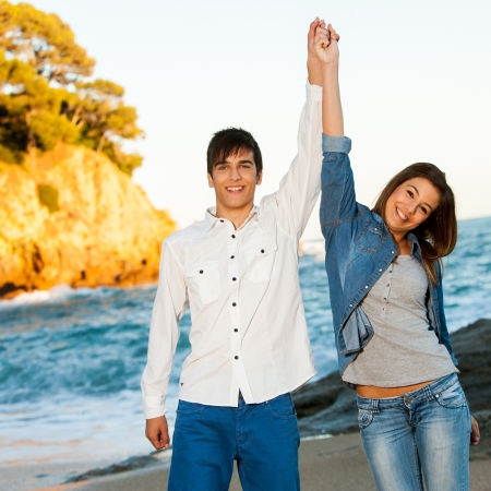 Portrait of happy young teen couple raising arms at seaside.の写真素材