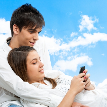 Close up portrait of cute teen couple socializing on smartphone outdoors.の写真素材