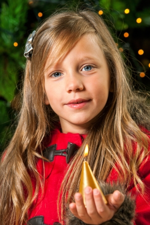 Cute blond girl holding golden candle at christmas tree の写真素材