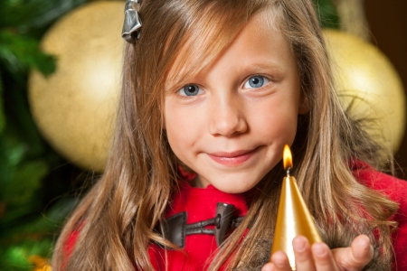 Portrait of cute little girl holding candle at christmas tree  の写真素材
