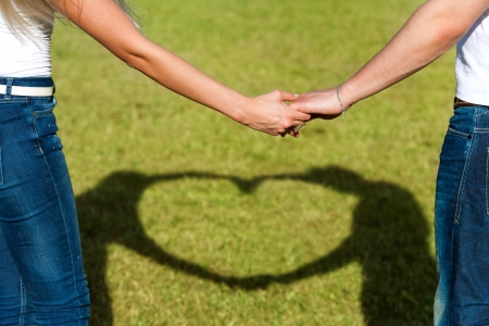 Close up of couples hands together with shadow of heart sign. の写真素材