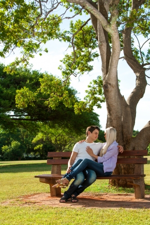 Portrait of young couple relaxing on wooden bench in park.の写真素材