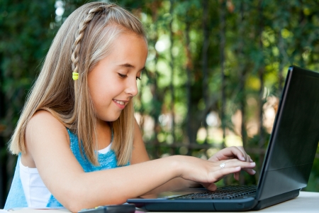 Portrait of young girl typing on laptop in garden.の写真素材