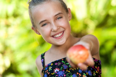 Close up portrait of cute young girl offering red apple outdoors.の写真素材