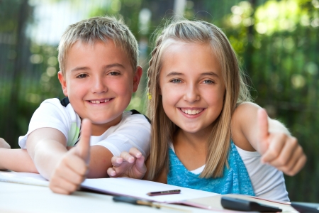 Two young students doing thumbs up at desk in garden.の写真素材