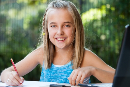 Close up portrait of cute girl student doing schoolwork in garden.の写真素材